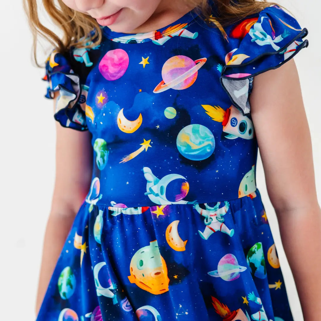 Close-up of a flutter-sleeve dress with a blue space print of planets, moons, astronauts, and shooting stars.